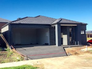 Modern single-storey charcoal brick home with double garage, tiled roof, and newly finished concrete driveway in a residential estate.
