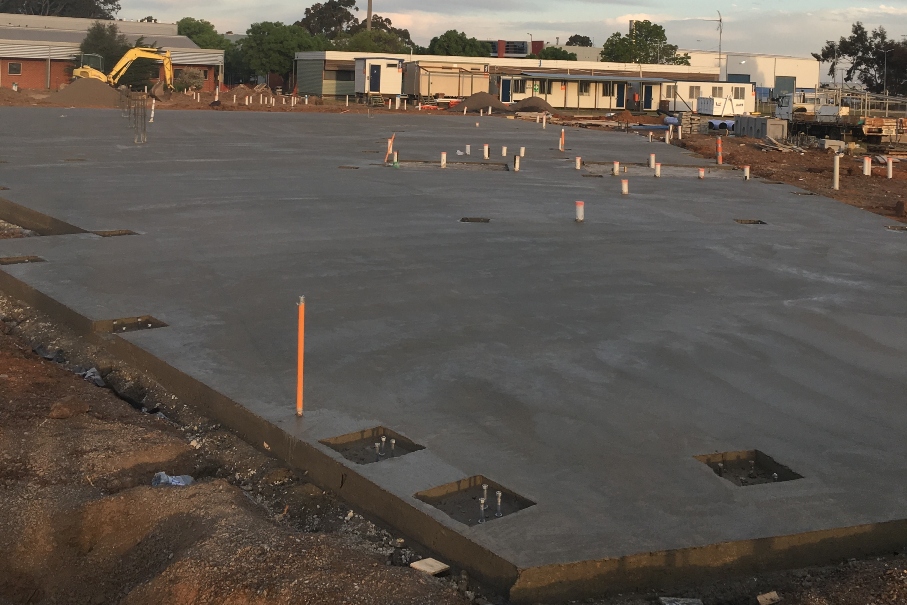 Freshly poured concrete slab foundation at a construction site with plumbing pipes in place, ready for the next stage of building.