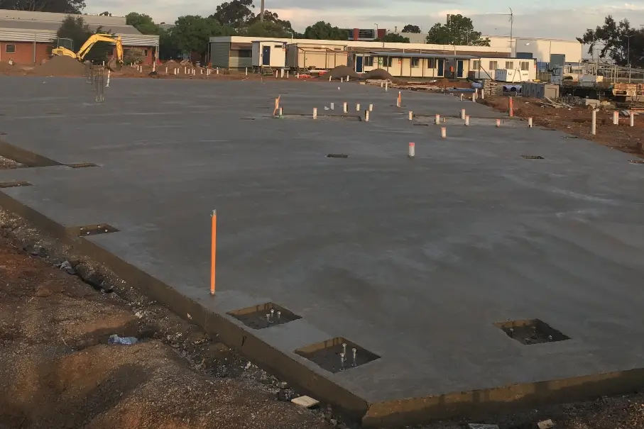 Freshly poured concrete slab foundation at a construction site with plumbing pipes in place, ready for the next stage of building.